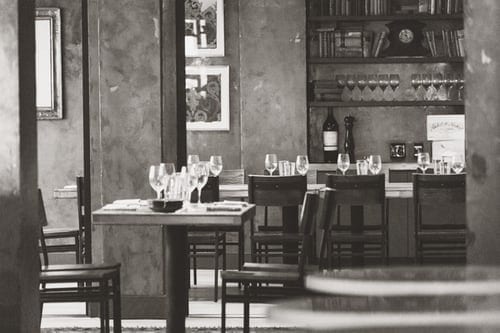 A sepia toned shot of several small tables in a wine bar. The tables are covered in used wine glasses.