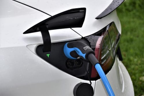 Rear, left-hand side view of a white electric car being charged, while plugged into a bright blue lead.