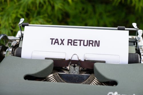 Close up of old-fashioned green, metal typewriter. Has a piece of paper in it with the words "Tax Return" as the heading.