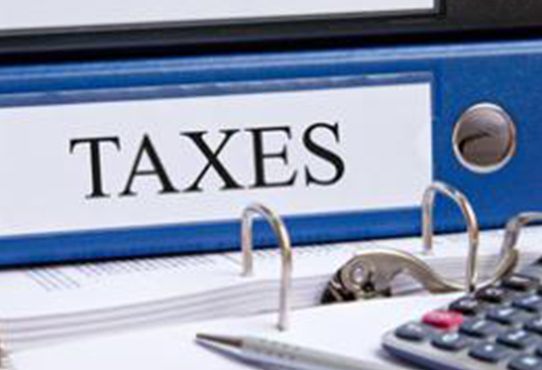 Bright blue folder, laying on its side, with the label "TAXES" running along its spine. The label is white and TAXES is written on bold black capitals. In front of that folder is another open folder and a calculator.