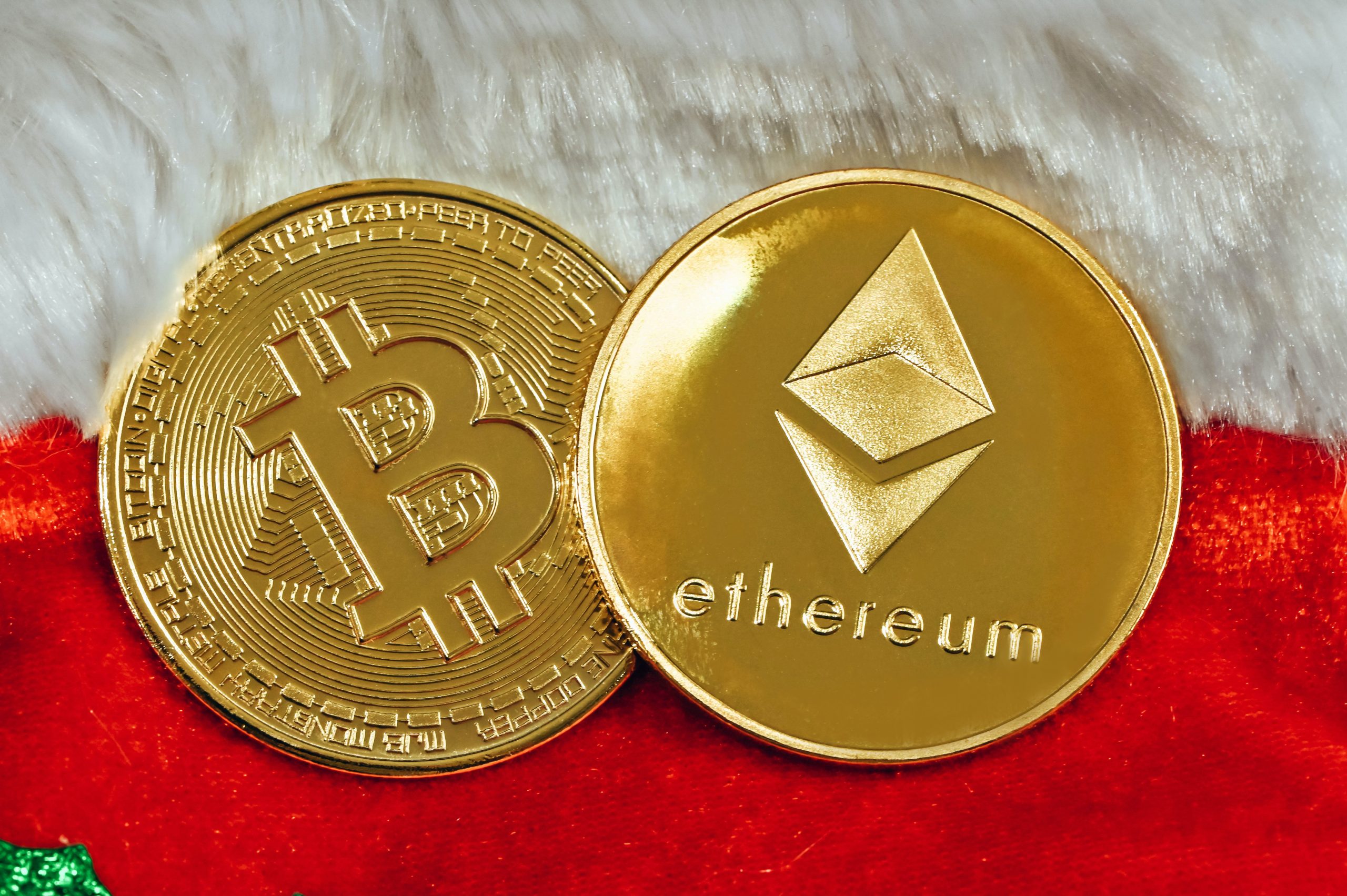 Close up of two gold cryptocurrency coins - Bitcoin and ethereum - sitting on a red cloth with white fur trim at it's edge.