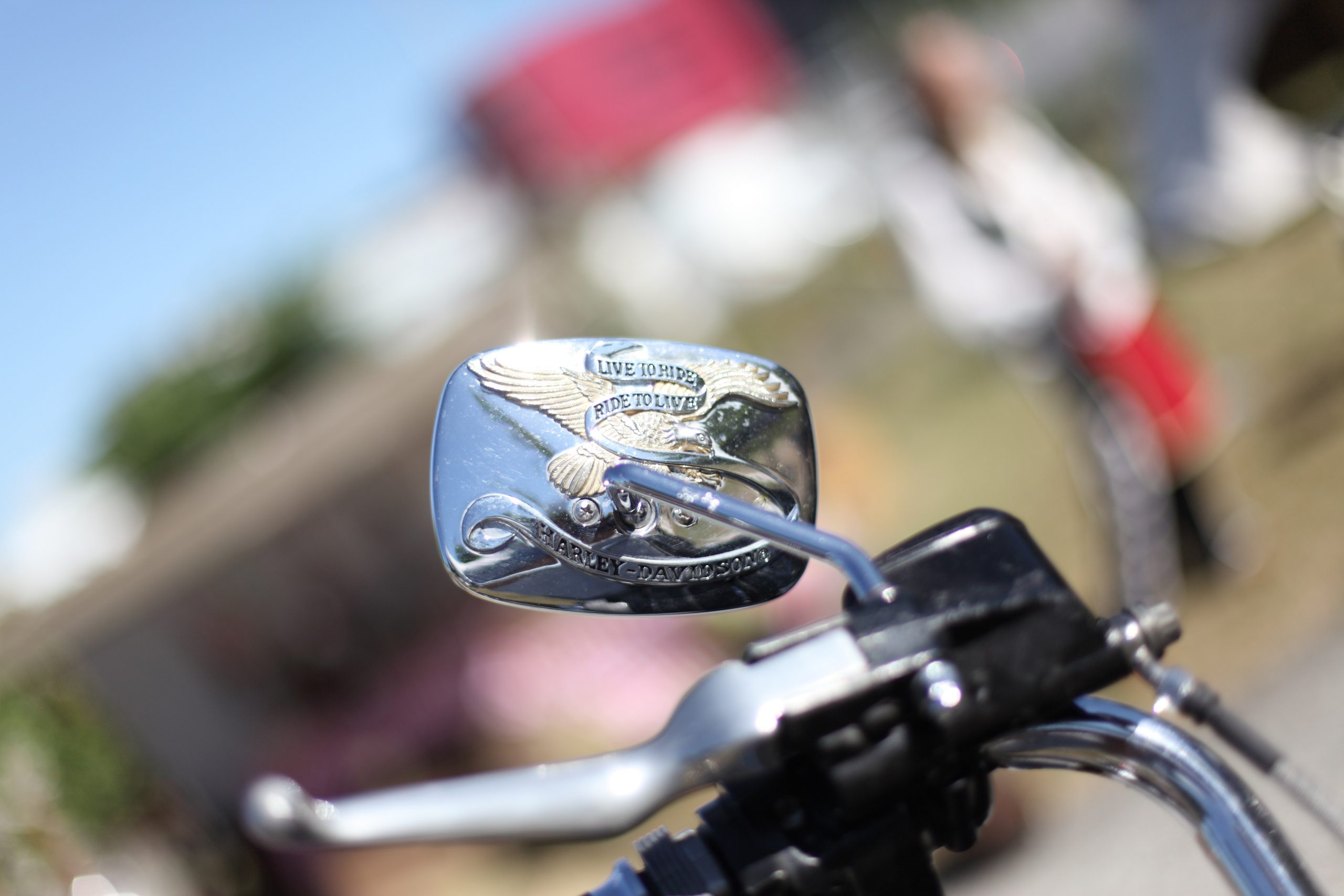 Close up of a Harley Davidson motor bike's wing mirror. Gold and chrome crest on the back of the mirror show the Harley slogan "Live to Ride, Ride to Live". The background is blurred, only the side mirror and part of the handlebar shows.