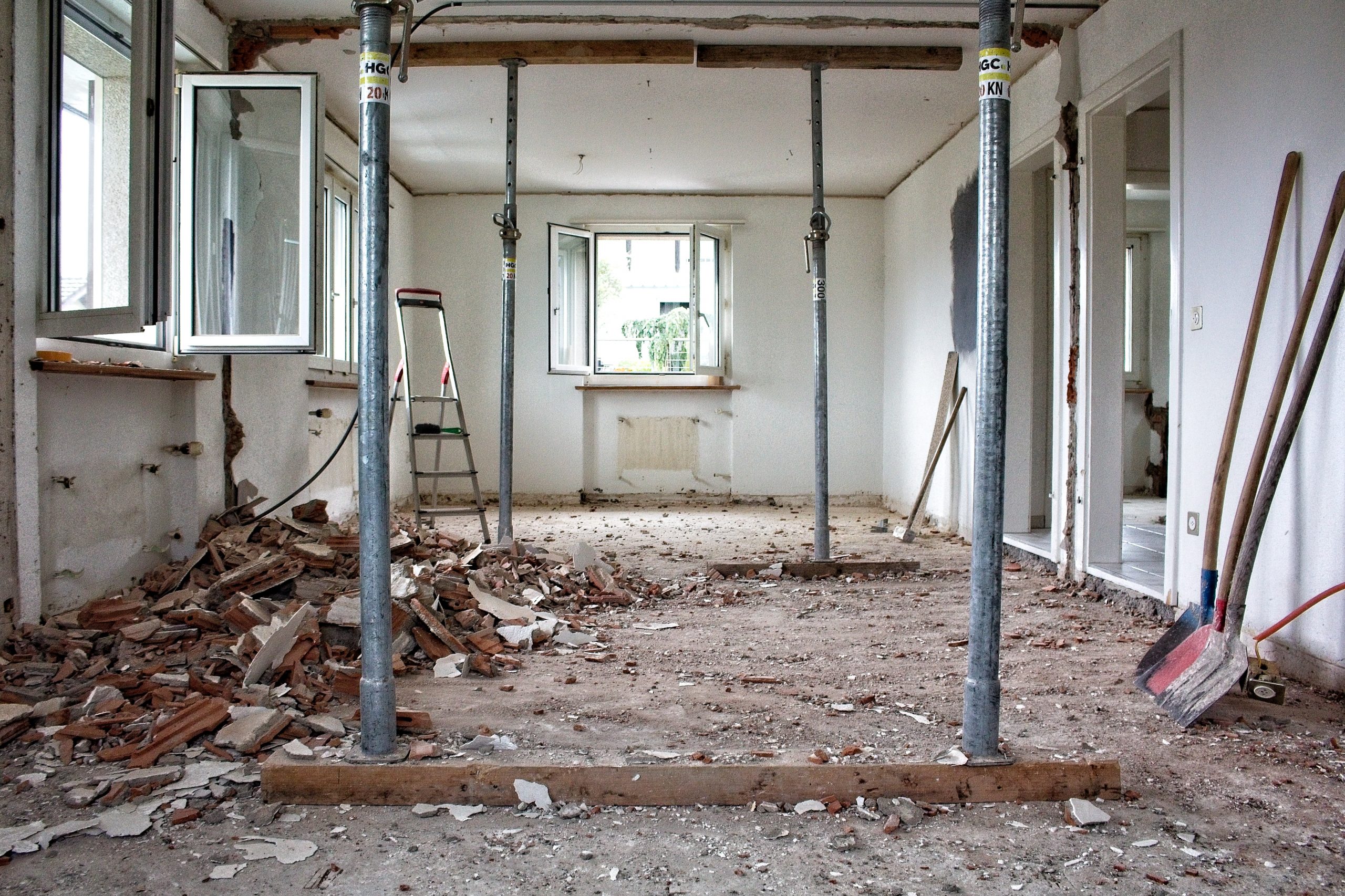 Room is being renovated and has been stripped out. Debris and bricks on floor, opens through to room next door, and ceiling being supported by Acrow props. Ladder, shovel, sledge hammer in view.