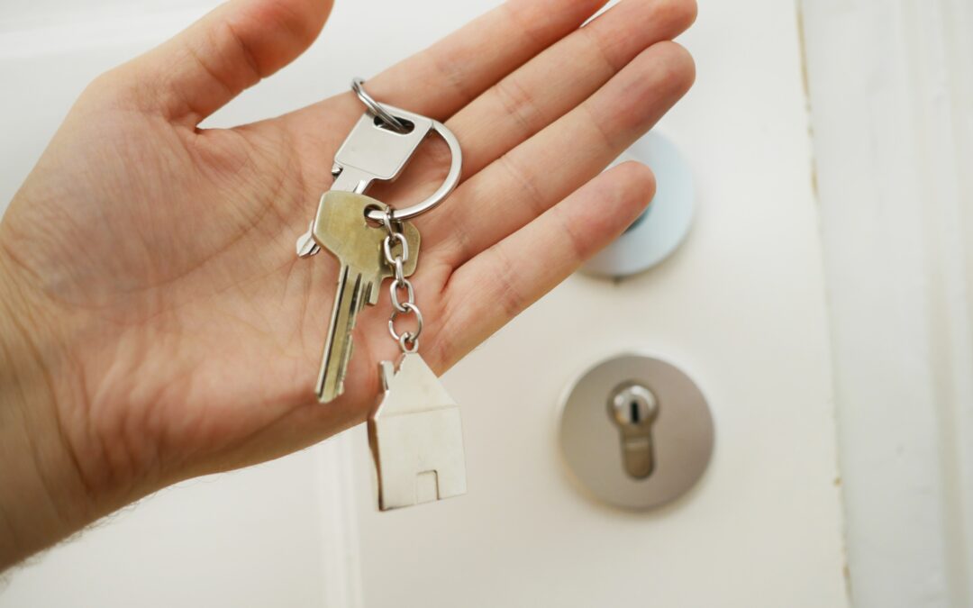 Hand holding keyring which contains two keys, as well as a small metal house on the fob.