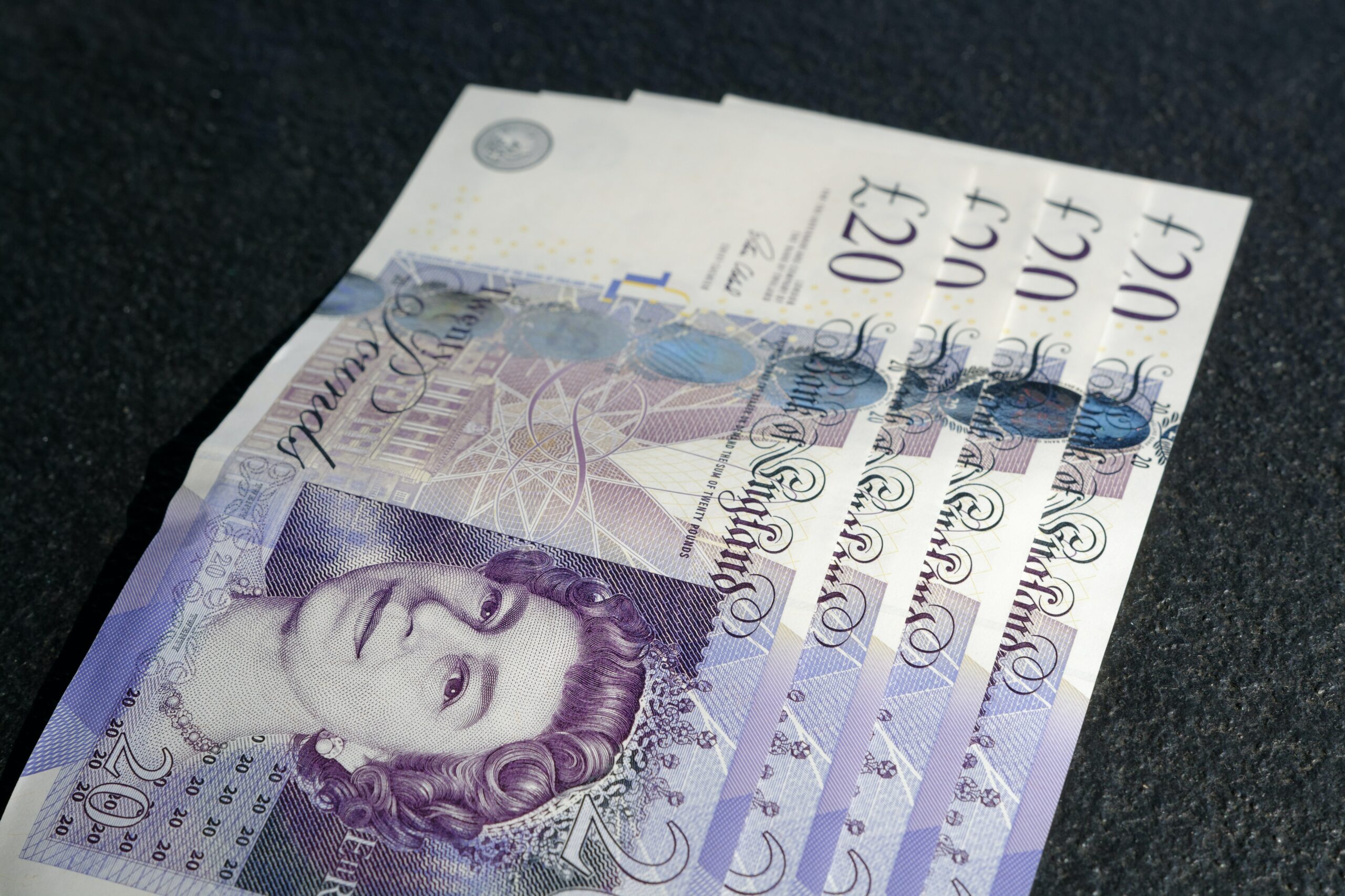 Four twenty pound notes, sitting slightly splayed out. They are purple and white sitting on a black background.