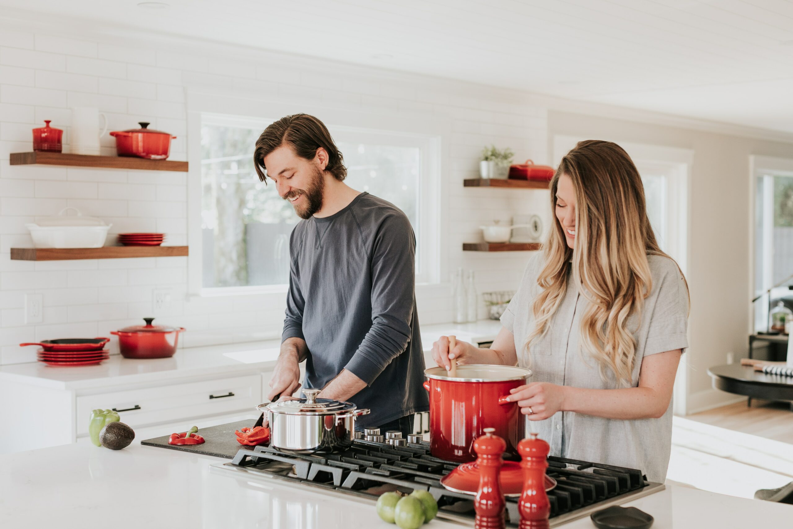 Young male and female standing cooking at stove top. Colour scheme of kitchen and crockery is red and white, pots on stove are red and chrome.