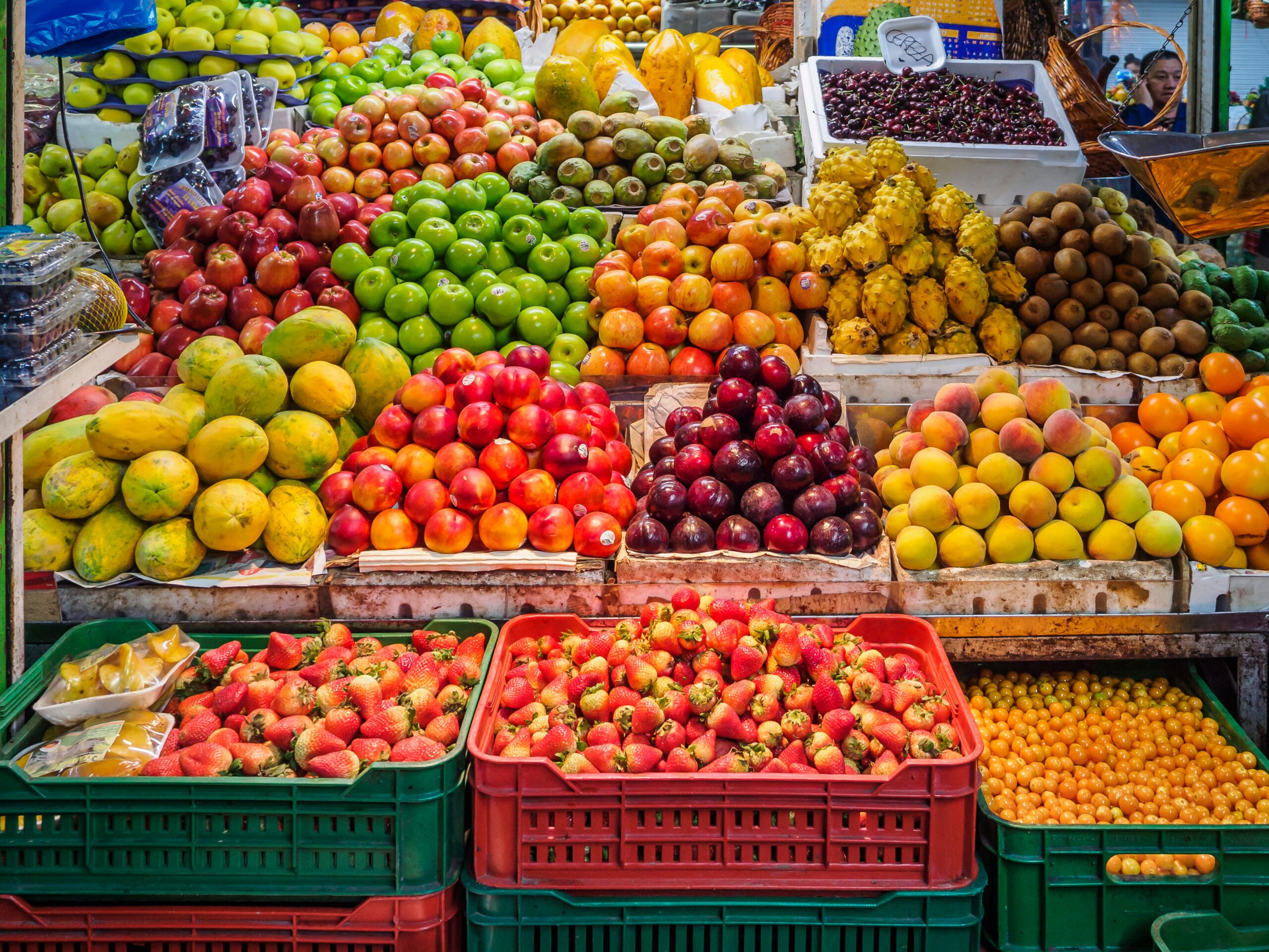 Fruit stall with abundance of fresh, bright fruit, including strawberries, plums, apples, cherries, kiwifruit, oranges and more