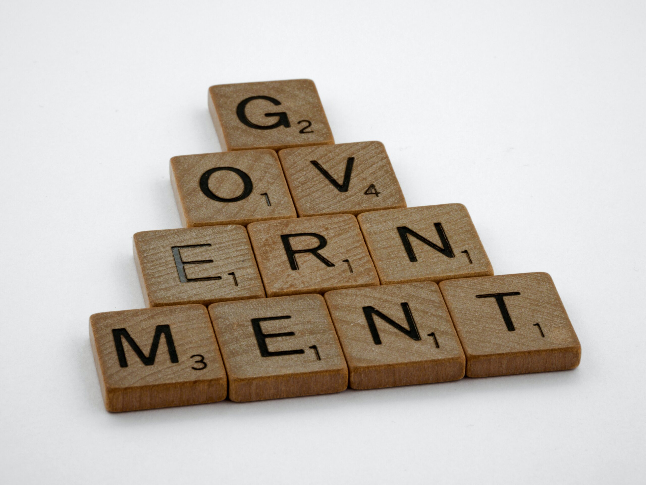 Government spelt out in Scrabble discs, formatted in a triangular shape, G at the top, OV underneath, ERN under that, and finally MENT on the bottom tier of the triangle