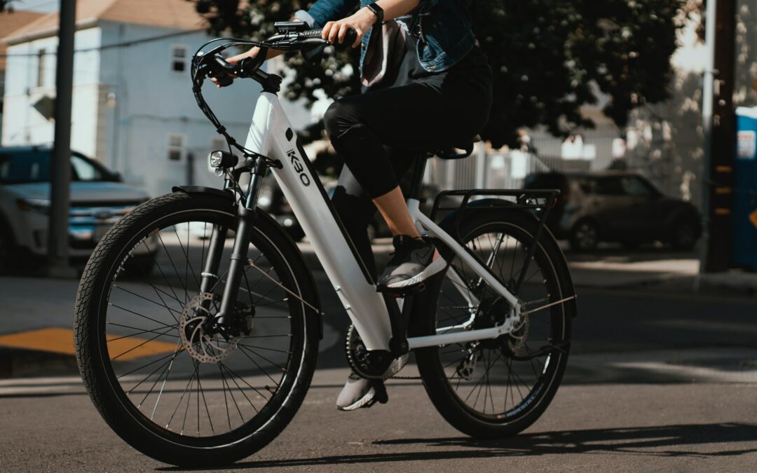 Close up of a woman on a black and white K30 electric bike, on a city street, wearing a denim jacket, grey shoes and black pants.