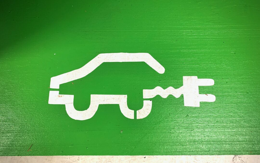 A drawing of an electric car charging, with a green background and car and electric plug drawn in white.