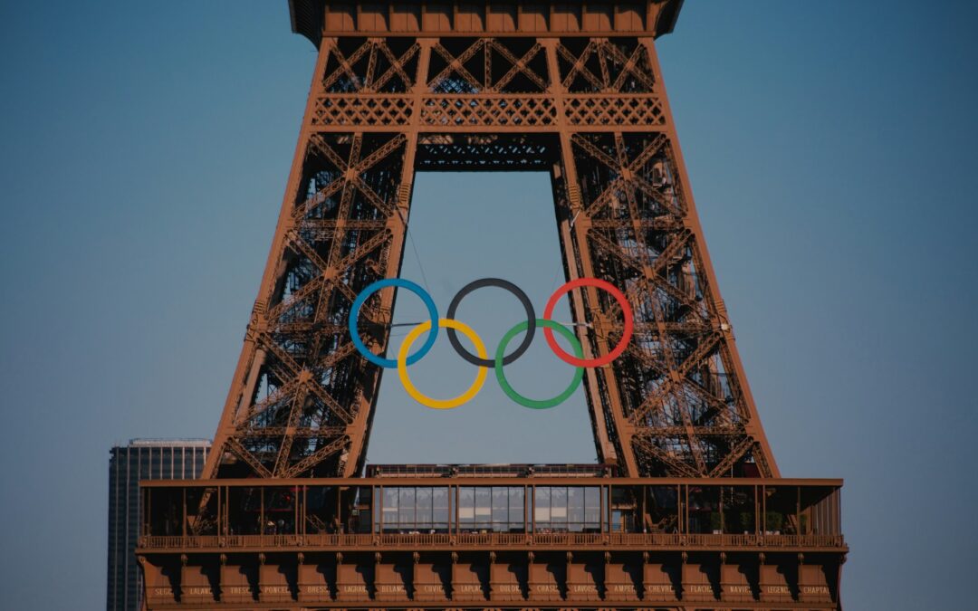 A close up view of the Eiffel tower, With the 5 rings of the Olympics logo strung across the front of the tower.