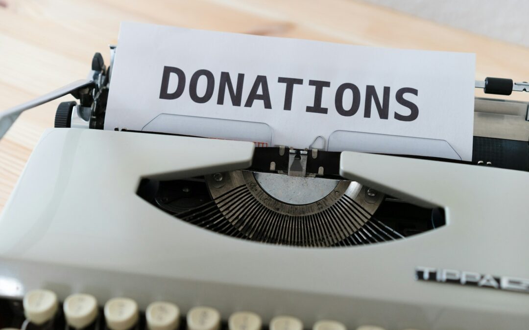 A piece of white paper sitting in an old-fashioned grey typewriter. It has the word "donations" typed on it in upper-case letters